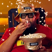 a man wearing glasses and a hat eating popcorn