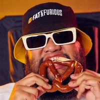 a man wearing sunglasses and a hat eating a pretzel